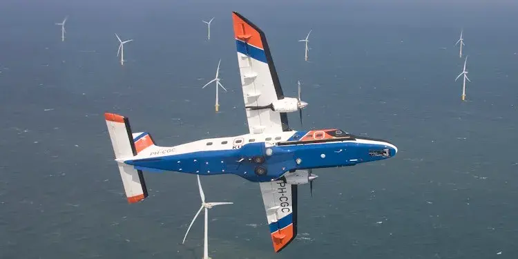 Airplane in the sky over the sea with wind turbines.