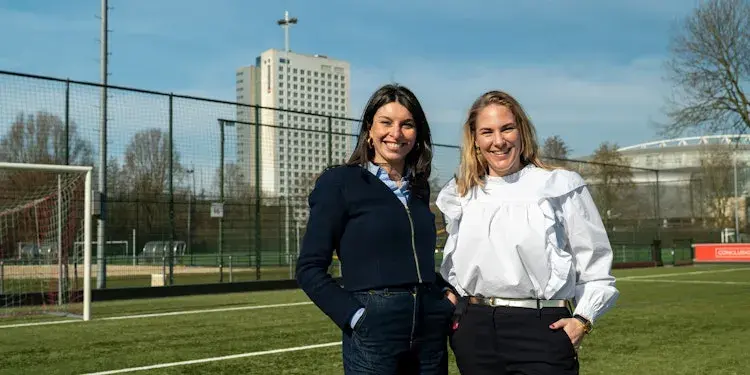 Two women on a soccer field in front of the Conclusion building.