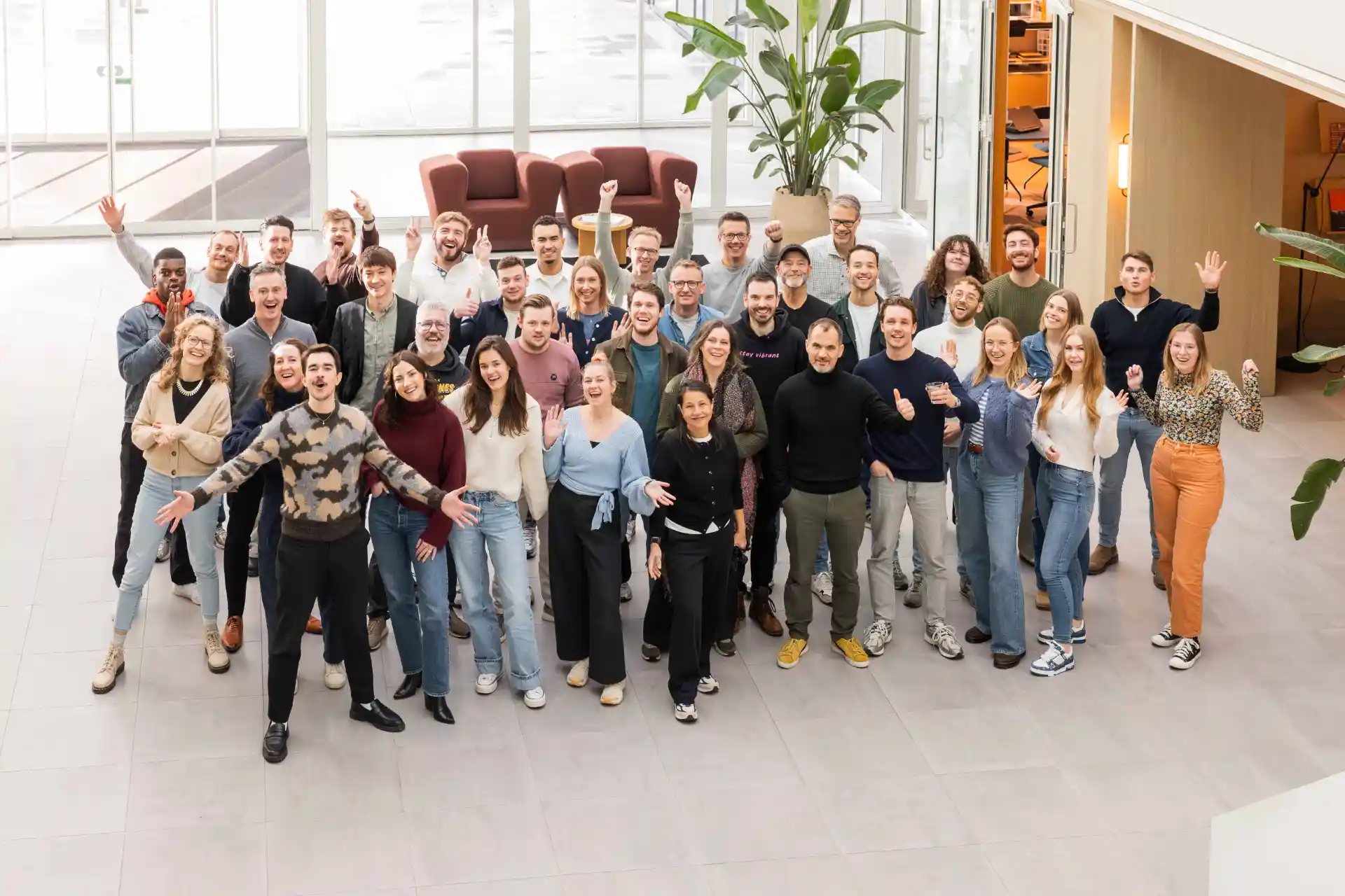 A large group of colleagues enthusiastically posing for a photo in a spacious, bright hall.