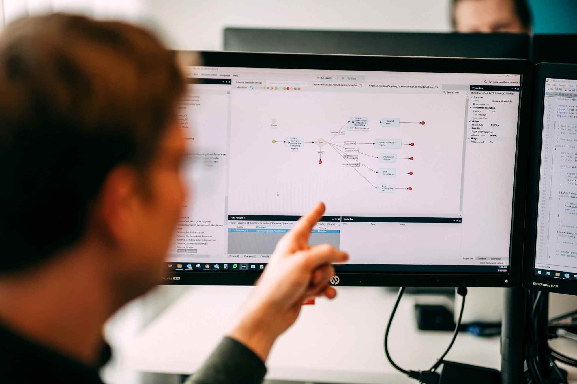 Man wijst naar een scherm met een visuele weergave van code en processen.
