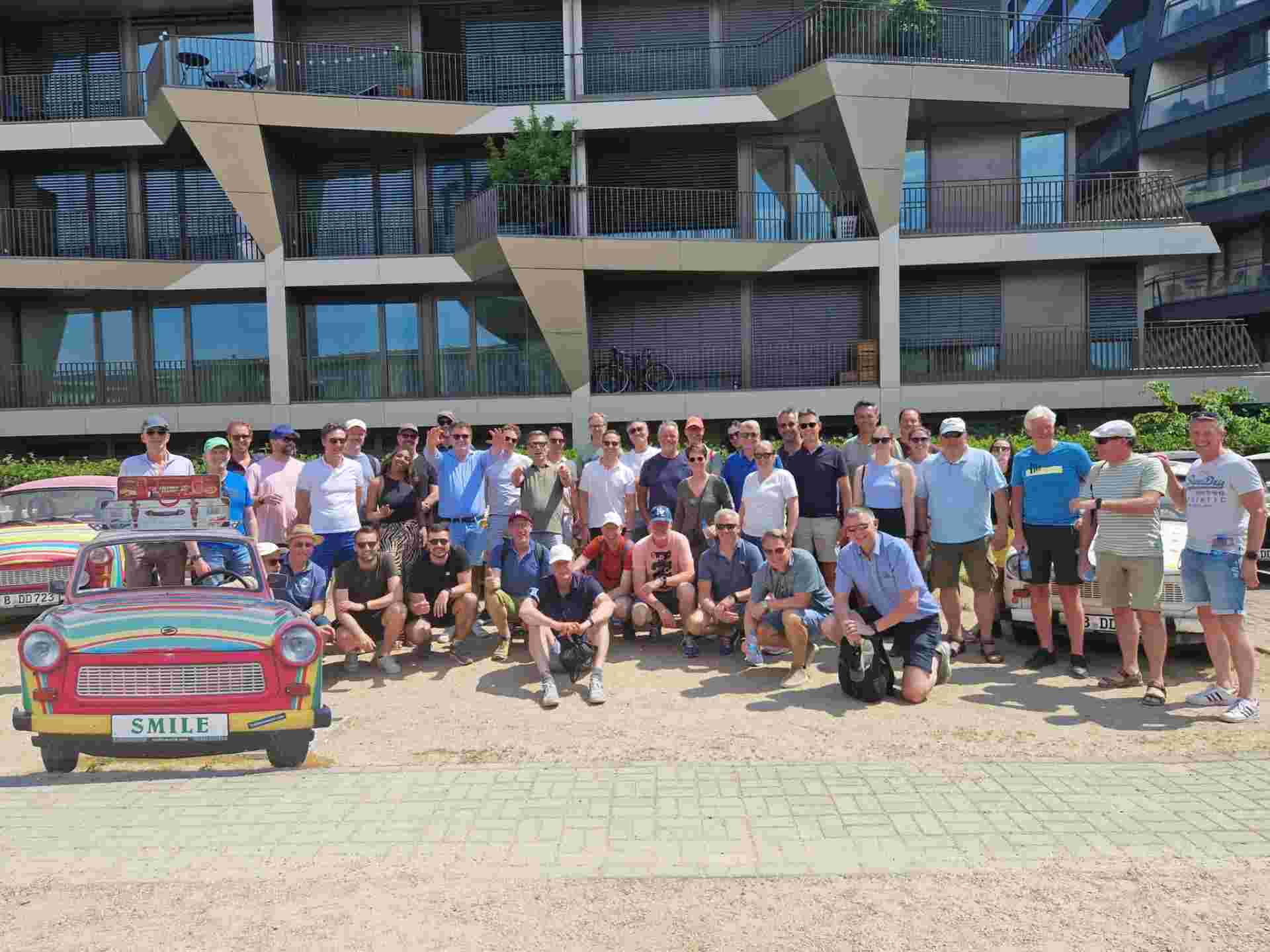 Groep mensen poseert voor een kleurrijke auto in de buitenlucht.